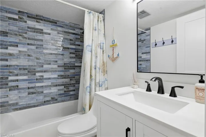 Bathroom vanity featuring a white rectangular under-mount sink, black faucet fixtures, and a white countertop