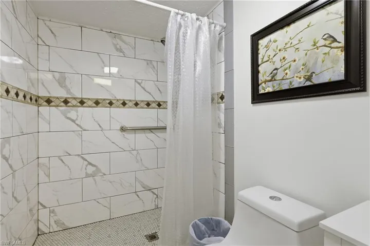 Shower stall featuring white subway tile with gray veining, a decorative mosaic tile accent band, and a white penny tile floor
