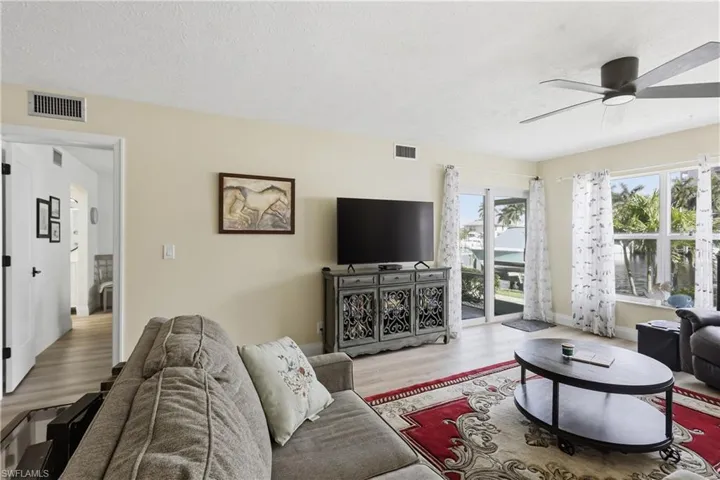 Living area featuring light wood-finish flooring, a contemporary ceiling fan, and ample natural light from multiple windows