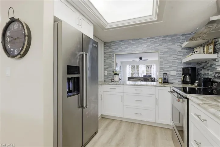Modern kitchen featuring stainless steel appliances, white cabinetry, a glass tile backsplash, light-colored countertops, and wood-finish flooring