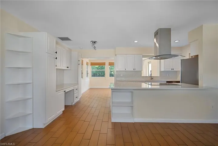 Kitchen featuring open shelves, white cabinetry, island exhaust hood, backsplash, and light stone counters