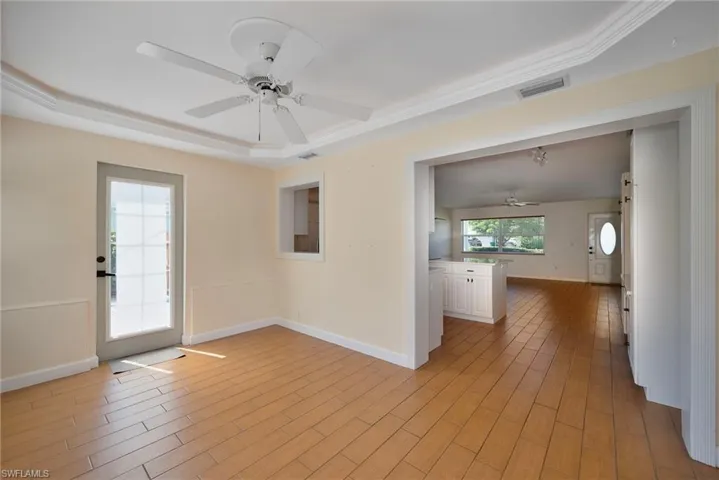 Empty room with a ceiling fan, light wood-type flooring, and a raised ceiling