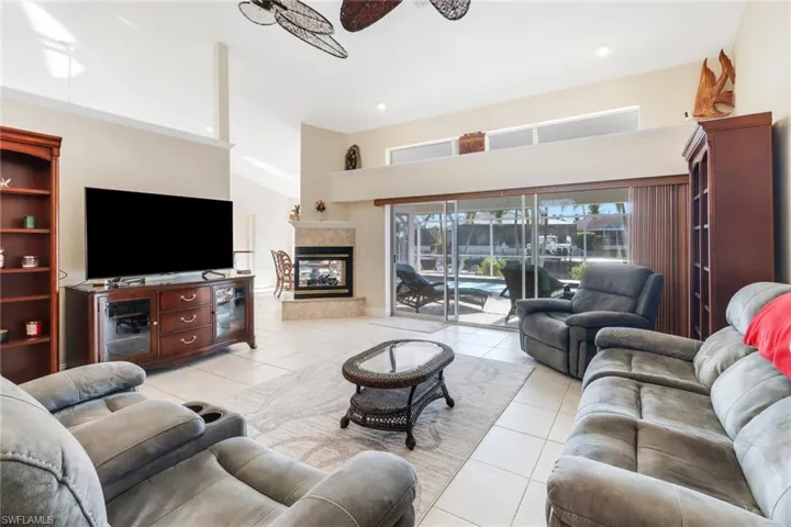 Tiled living room with ceiling fan, a towering ceiling, and a tile fireplace