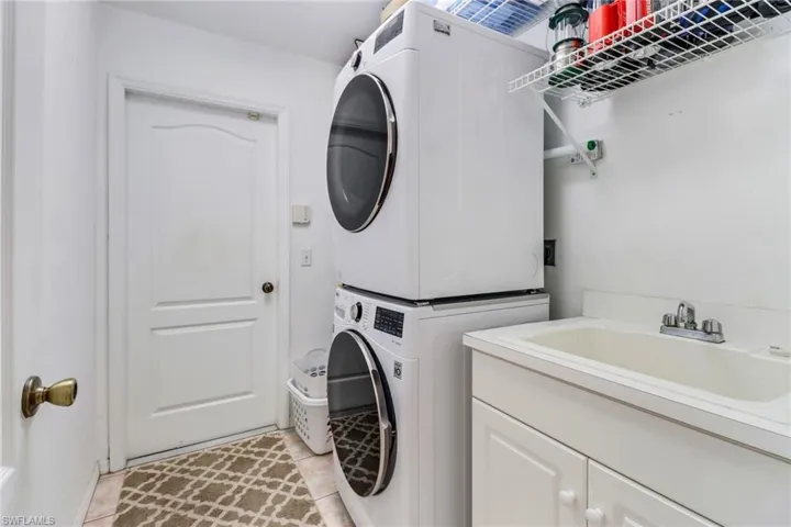 Washroom with cabinets, light tile patterned floors, stacked washing maching and dryer, and sink