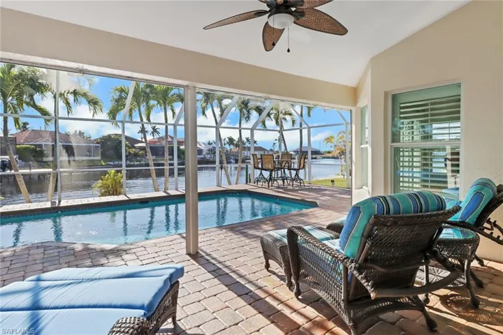 View of pool with a lanai, ceiling fan, a patio area, and a water view