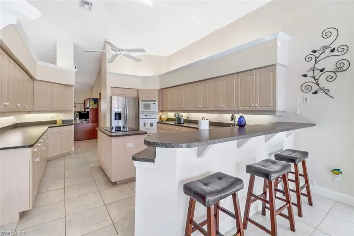 Kitchen featuring a kitchen island, a kitchen breakfast bar, kitchen peninsula, white appliances, and light tile patterned floors