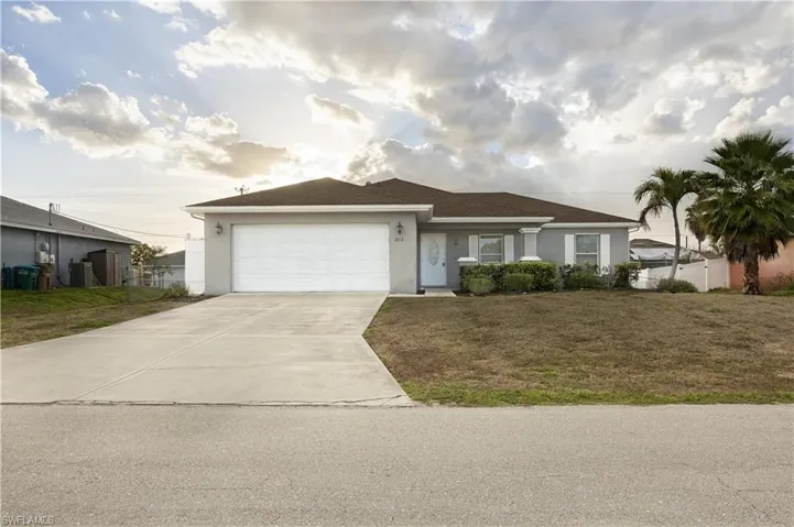 Ranch-style home with stucco siding, an attached garage, a front yard, and concrete driveway