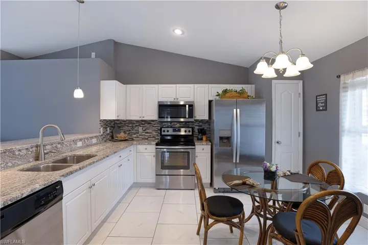 Kitchen featuring stainless steel appliances, light stone counters, white cabinets, suspended lighting, and lofted ceiling