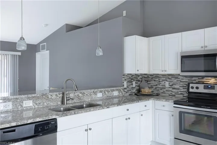 Kitchen featuring stainless steel appliances, light stone countertops, white cabinetry, lofted ceiling, and hanging light fixtures