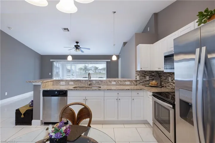 Kitchen with stainless steel appliances, pendant lighting, light stone countertops, white cabinets, and lofted ceiling