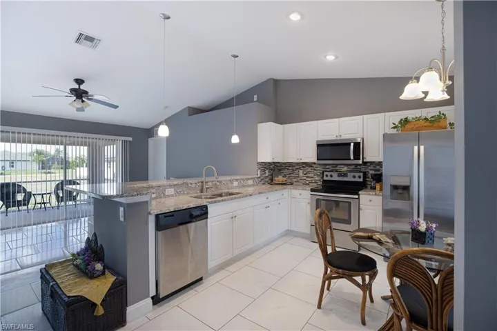 Kitchen featuring stainless steel appliances, white cabinets, light stone countertops, a peninsula, and decorative backsplash