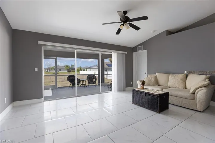 Living room with ceiling fan, light marble finish flooring, and vaulted ceiling