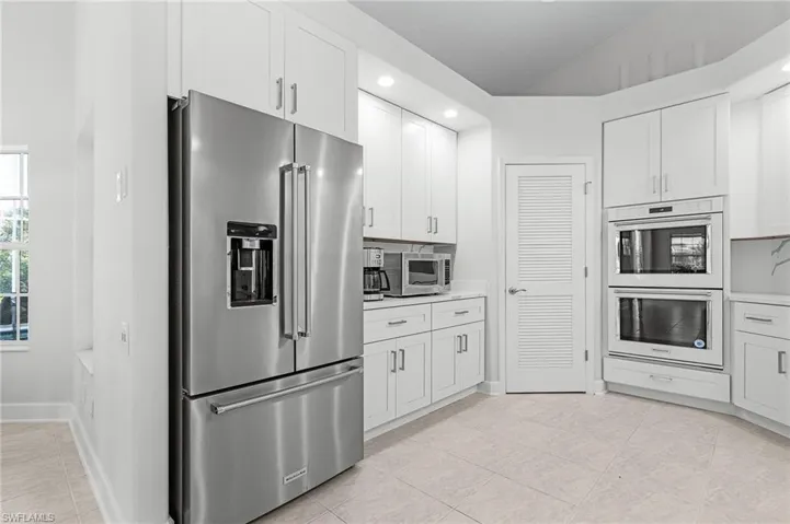 Kitchen with appliances with stainless steel finishes, vaulted ceiling, white cabinets, light tile patterned floors, and recessed lighting