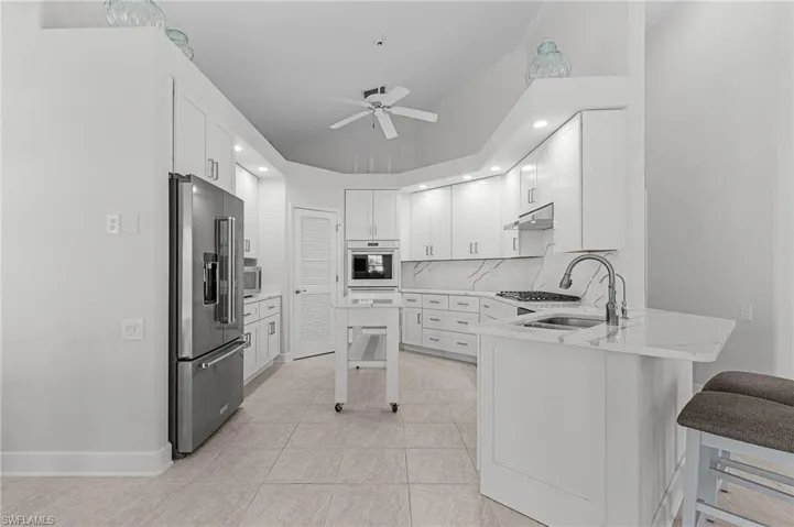 Kitchen with appliances with stainless steel finishes, under cabinet range hood, a peninsula, ceiling fan, and a kitchen breakfast bar