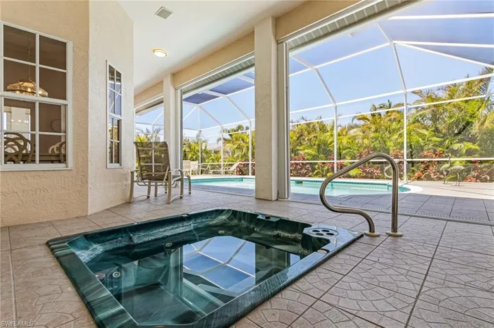 Outdoor pool featuring an in-ground hot tub, a patio, and glass enclosure