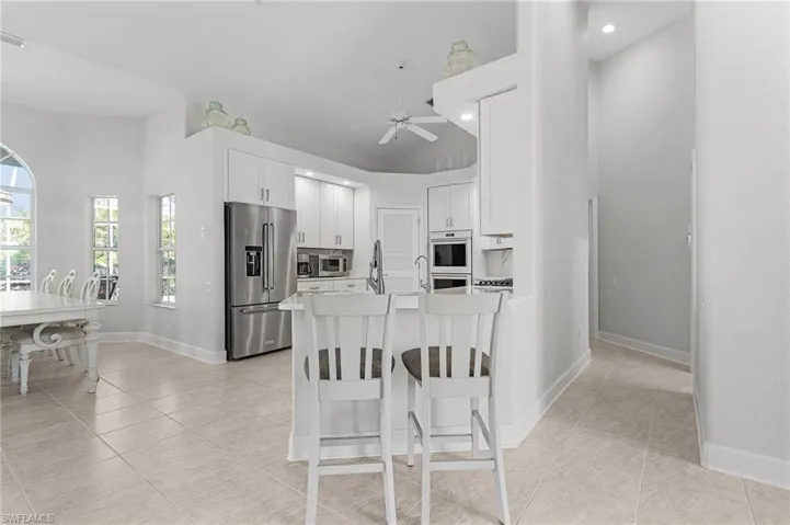 Kitchen with stainless steel appliances, light tile patterned floors, a ceiling fan, a breakfast bar area, and recessed lighting