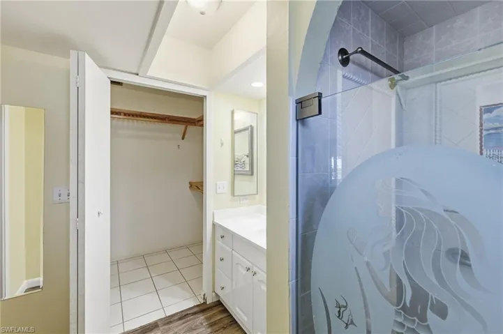 Full bath featuring vanity, a spacious closet, walk in shower, and wood finished floors
