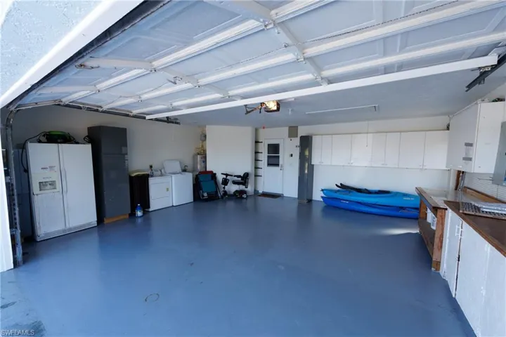 Garage featuring white fridge with ice dispenser, washing machine and clothes dryer, electric panel, and water heater