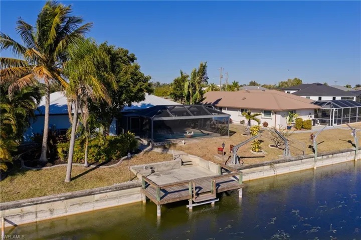 Dock area with glass enclosure, a sunroom, boat lift, a lawn, and a water view