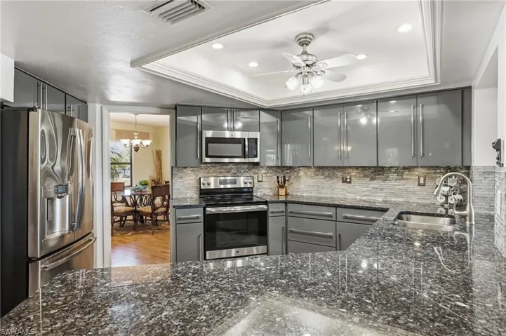 Kitchen featuring gray cabinetry, dark stone countertops, stainless steel appliances, a ceiling fan, and crown molding