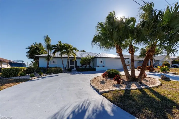 Ranch-style home with curved driveway, an attached garage, a metal roof, and stucco siding
