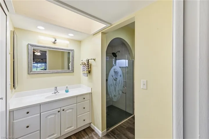 Full bath with a shower stall, vanity, dark wood-type flooring, and recessed lighting