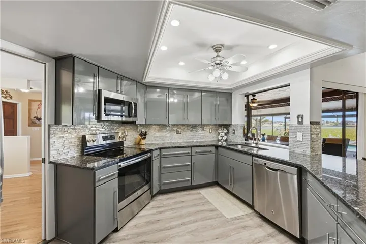 Kitchen with gray cabinets, stainless steel appliances, light wood-type flooring, dark stone counters, and recessed lighting