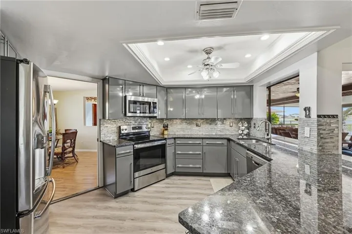 Kitchen with gray cabinetry, stainless steel appliances, dark stone countertops, light wood finished floors, and ceiling fan