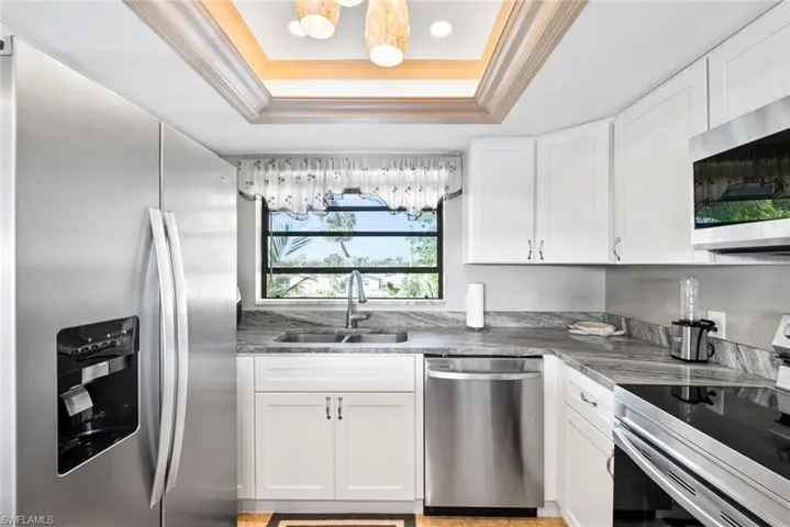 Kitchen with a tray ceiling, stainless steel appliances, crown molding, white cabinetry, and a sink