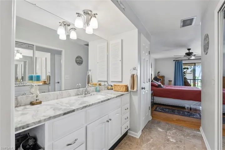 Ensuite bathroom with visible vents, connected bathroom, vanity, baseboards, and ceiling fan with notable chandelier