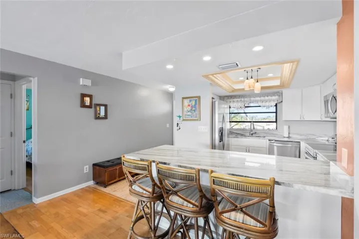 Kitchen featuring a raised ceiling, appliances with stainless steel finishes, a sink, light stone countertops, and a peninsula