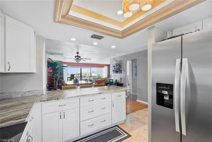 Kitchen with a tray ceiling, crown molding, visible vents, a peninsula, and stainless steel fridge with ice dispenser
