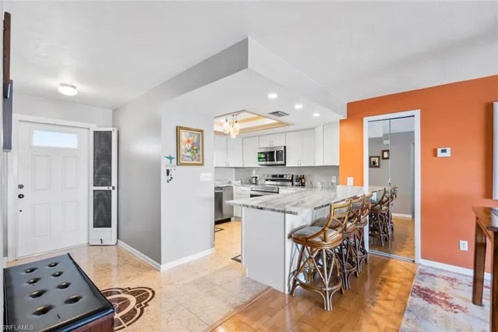 Kitchen featuring baseboards, a peninsula, stainless steel appliances, a kitchen bar, and white cabinetry