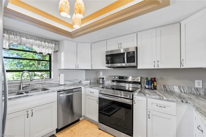 Kitchen with stainless steel appliances, a tray ceiling, a sink, and white cabinetry