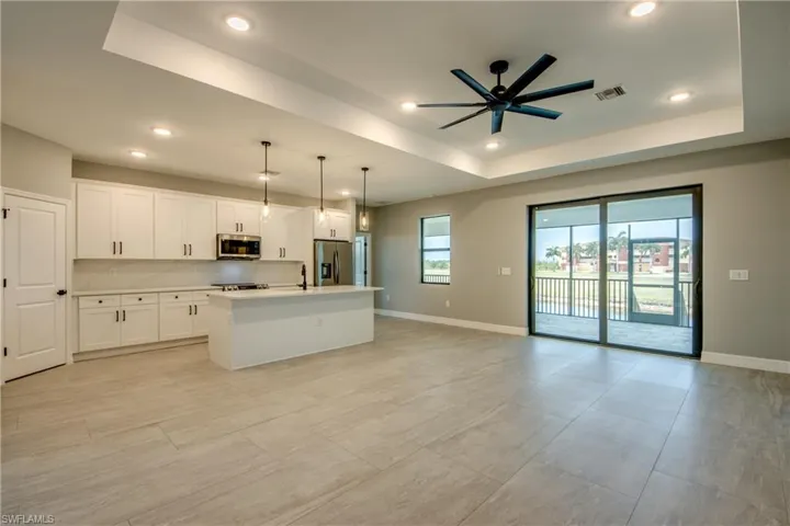 Kitchen featuring appliances with stainless steel finishes, an island with sink, decorative light fixtures, ceiling fan, and a raised ceiling