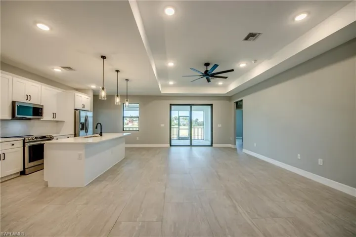 Kitchen with stainless steel appliances, an island with sink, ceiling fan, light tile floors, and a raised ceiling