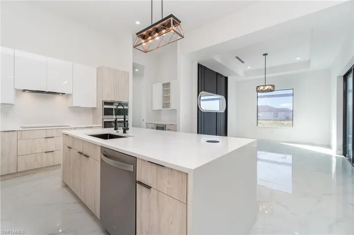 Kitchen featuring sink, decorative light fixtures, a center island with sink, and light brown cabinetry