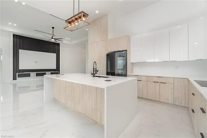 Kitchen featuring a kitchen island with sink, sink, black appliances, decorative light fixtures, and white cabinetry