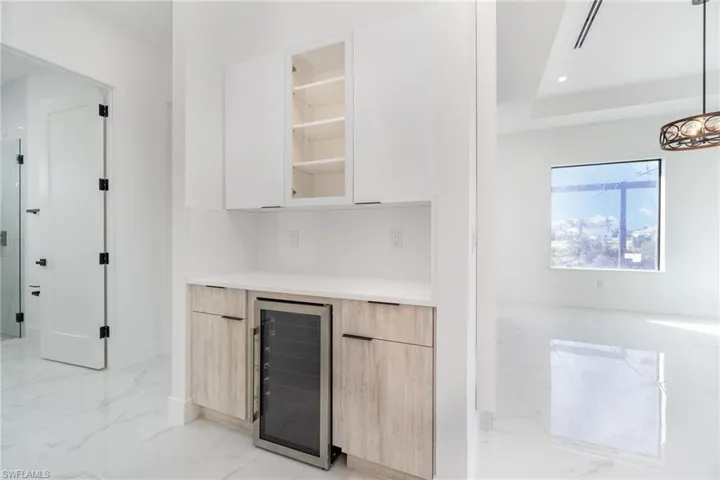 Bar featuring wine cooler, white cabinets, hanging light fixtures, light brown cabinetry, and a tray ceiling