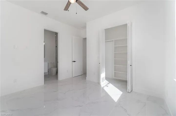 Unfurnished bedroom with a spacious closet, a closet, ensuite bath, and ceiling fan