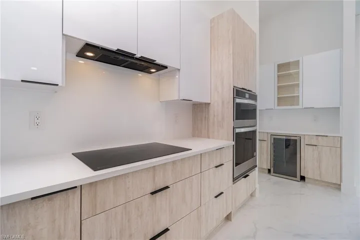 Kitchen featuring light brown cabinetry, black electric cooktop, white cabinets, range hood, and wine cooler