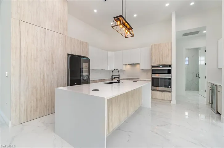 Kitchen featuring double oven, a kitchen island with sink, black refrigerator, sink, and pendant lighting