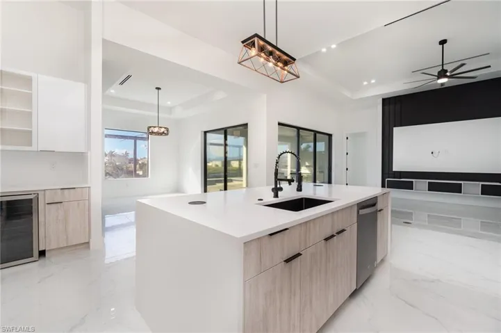 Kitchen with sink, an island with sink, a tray ceiling, and beverage cooler