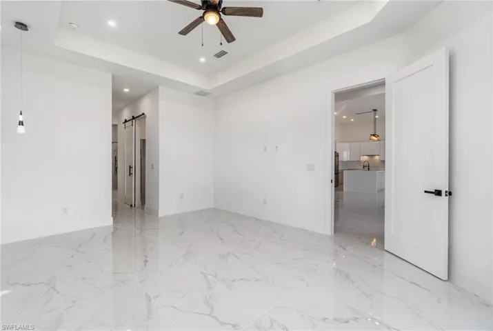 Unfurnished room with a barn door, ceiling fan, and a raised ceiling