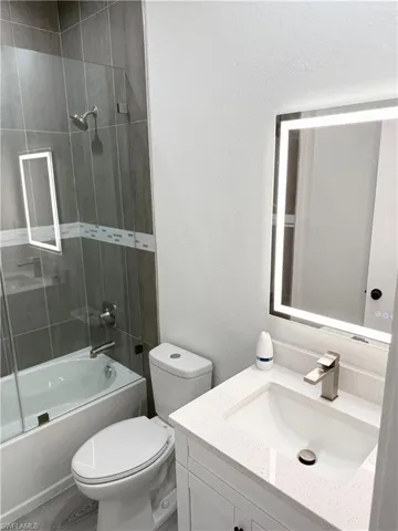 Bathroom with vanity, bath / shower combo with glass door, a textured wall, and wood finished floors