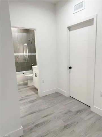 Full bath featuring combined bath / shower with glass door, light wood-style flooring, and vanity