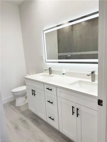 Bathroom with double vanity, light wood finished floors, and a textured wall