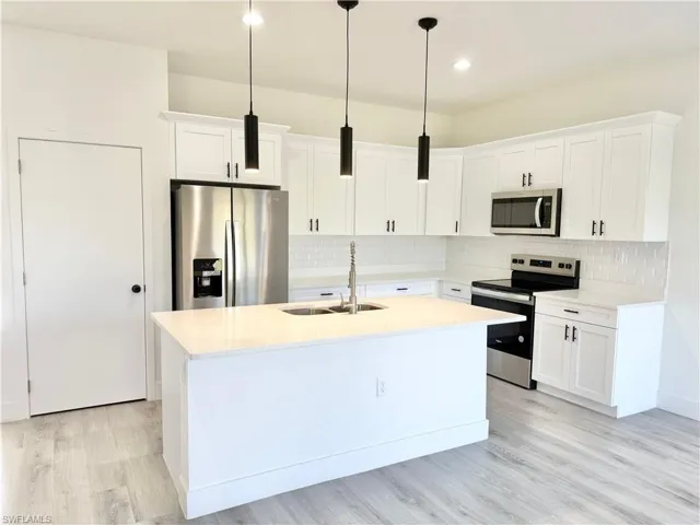 Kitchen featuring stainless steel appliances, white cabinetry, light stone countertops, a kitchen island with sink, and light wood-style flooring