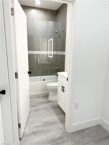 Full bath featuring vanity, light wood-type flooring, and combined bath / shower with glass door