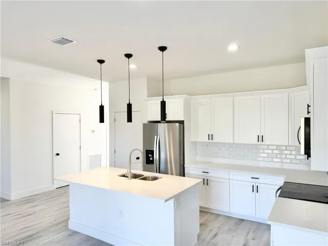 Kitchen with stainless steel appliances, a kitchen island with sink, light stone counters, decorative light fixtures, and white cabinetry